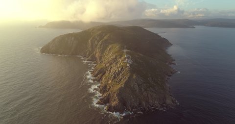 Aerial: Clouds moving over Cape Finisterre Lighthouse on mountain in sea during sunset