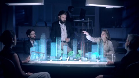 In the Near Future: Businessman in Suit presenting Architecture Project to Colleagues and Partners sitting around Futuristic Table with Holographic Modern Augmented Reality Technology.