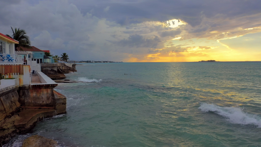 Aerial: Golden Sunset Behind Clouds Over Tropical Water, Three People Swimming Near Waterfront Homes - Nassau, Bahamas