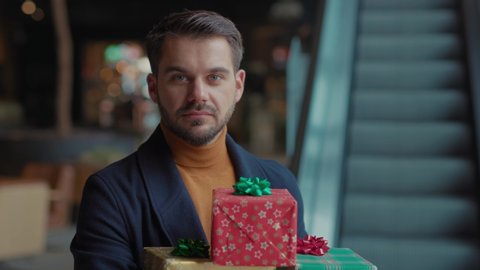 Face of young attractive man with Christmas presents smiling, looking at camera. slow motion