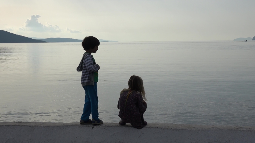 Akyaka, Mugla, Turkey - 9th of November 2019: 4K Trekking shot walking children and fish splash in the sea at dusk
