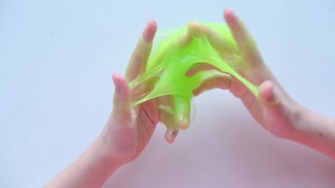 Girl stretching green slime to the sides. kids hands playing slime toy. Making slime on white. Trendy liquid toy sticks to hands and fingers. 4k footage.