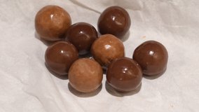 Slow motion video of dark and milk chocolate covered balls falling down. Malted milk balls on white paper. Round candy caramel. 4K, full hd video. Selective focus.