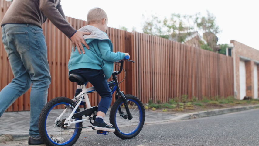 Dad help support son balance on bike, learning how to ride bicycle giving a push on the back Royalty-Free Stock Footage #1041623971