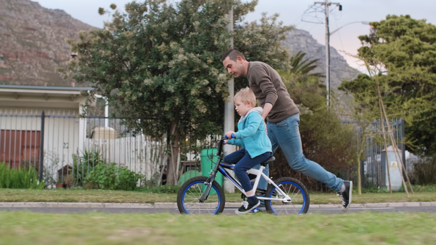Father running teaching his son how to cycle ride a bicycle, helping balance Royalty-Free Stock Footage #1041623992