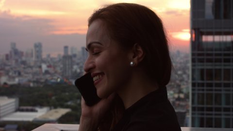 young smiling woman on the phone, in the background, a sunset over the city and buildings of Manila Philippines