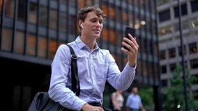 Caucasian male entrepreneur in formal clothing using roaming internet connection for making phone video call via international application on smartphone, employee in earphones communicating outdoors
