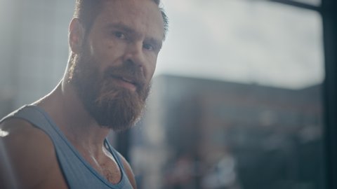 Portrait of Strong Bearded Male Athlete Wearing Sleeveless Shirt Wipes Sweat From His Forehead with His Muscular Hand. Handsome Man after Hardcore Exercise and Training. Man Gets Job Done