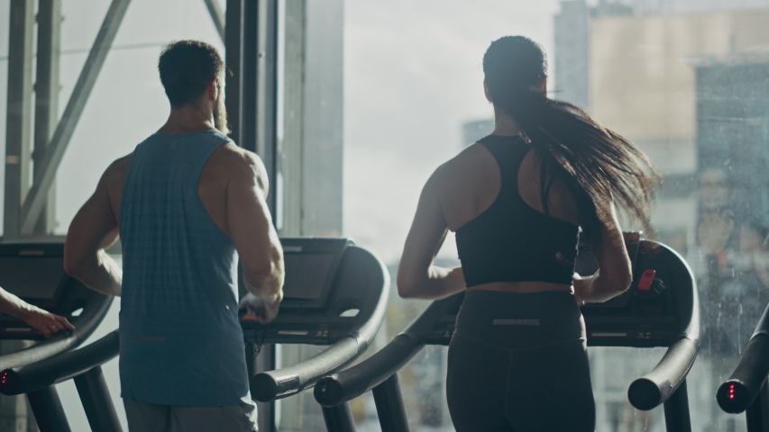 Male and Female Couple Exercising on Treadmills, Doing Fitness Exercise. Muscular Athletes Actively Training in the Modern Gym. Sports People Workout in Luxury Fitness Club. Back View Slow Motion Royalty-Free Stock Footage #1041637675