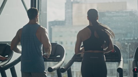 Male and Female Couple Exercising on Treadmills, Doing Fitness Exercise. Muscular Athletes Actively Training in the Modern Gym. Sports People Workout in Luxury Fitness Club. Back View Slow Motion