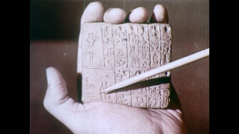 1950s: Sumerian cuneiform writing, hand holds clay tablet, points with sharp wooden stick to symbols in vertical columns.