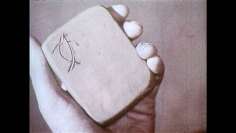 1950s: Sumerian cuneiform writing, Hand holds clay tablet, presses flat edge of wooden stick to print lines, symbols.