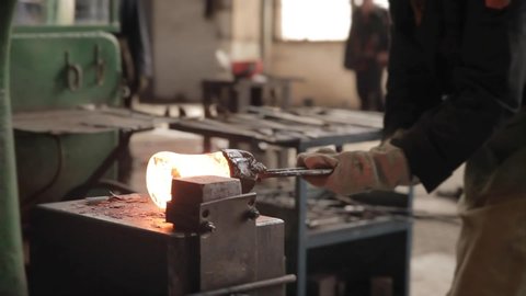 Forging hammer works. The process of forging metal. The billet of red-hot metal in the blacksmith's tongs, after heating in an industrial furnace, is processed by a hydraulic press