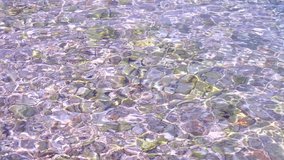 Beautiful seabed with stones. Pink, violet tinted sea water shimmers in shallow waves sun and creates sun glare. Sea Screensaver for spa, relaxation. Video vacation, summer vacation. Sea background.