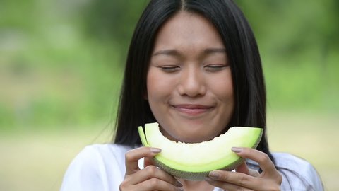 Asian women hold melon in hands and eat deliciously. face expression licking. Melon is a sweet fruit that makes her eat gluttonously. Girl enjoying eat melon with a delicious taste sweet and fragrant.