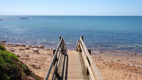 POV forward walk down on wooden stairs leading to secluded ocean beach with beautiful shallow turquoise water in Australia