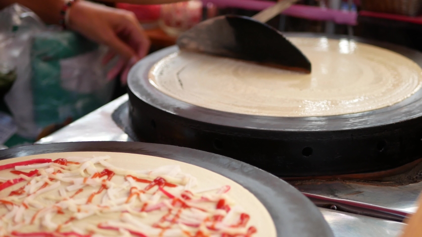 A thin egg-rich batter being spread and cooked into a large, thin cake on the stovetop / a crepe maker - making crepes