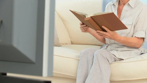 Senior Caucasian woman reading a book on her sofa