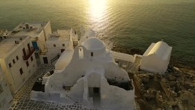 Aerial drone video landmark church of Paraportiani overlooking the Aegean sea in main village of Mykonos island at sunset with beautiful colours, Cyclades, Greece