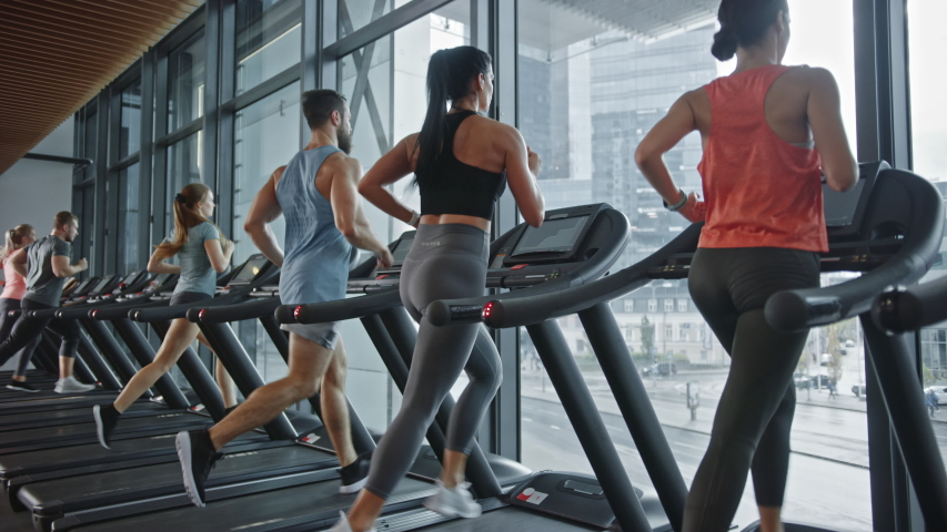Group of Six Athletic People Running on Treadmills, Doing Fitness Exercise. Athletic People Actively Workout in the Modern Gym. Sports People Workout in Fitness Club. Side View Slow Motion