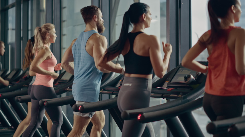 Athletic People Running on Treadmills, Doing Fitness Exercise. Athletic and Muscular Women and Men Actively Training in the Modern Gym. Sports People Workout. Back View Elevating Camera Royalty-Free Stock Footage #1041686350