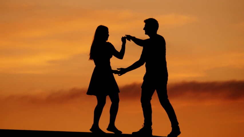 Happy couple dancing silhouettes against yellow sunset sky, telephoto perspective. Man and woman make series of swingout moves, moderate slow motion shot Royalty-Free Stock Footage #1041688843