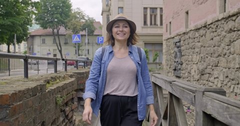 Smiling middle-aged woman walking in an old tourist town. Happy female raises her arms to the sky