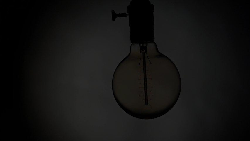 Swaying and flashing Edison light bulb over dark background. Flickering old retro light bulb lamp. Power outages concept UHD, 4K Royalty-Free Stock Footage #1041690271