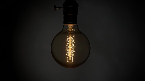 Swaying and flashing Edison light bulb over dark background. Flickering old retro light bulb lamp. Power outages concept UHD, 4K