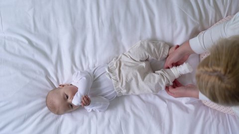 Babysitter carefully dressing newborn baby in soft cotton clothes, love and care