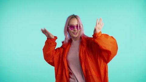 Young attractive american hipster woman in orange raincoat enjoying life and dancing at blue background. Music, lifestyle, modern fashion concept. 4k