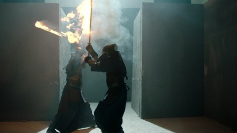 Japanese kendo fighters with burning swords competing in the fog in dark mystic industrial building . Super mystical video . Battle of two kendo fighter with fire sword . Shot on ARRI Alexa Camera .