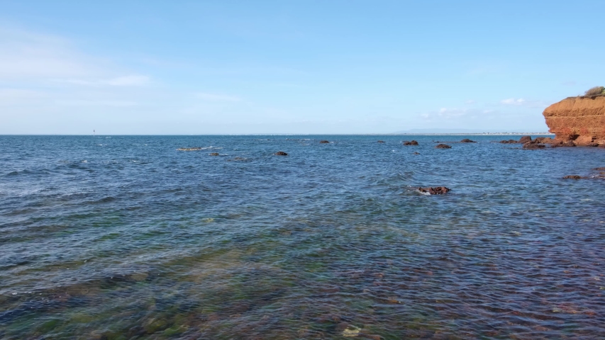 Pan across shallow bay waters leading to rocky outcrops of the coastline. Mornington Peninsula, Victoria, Australia.