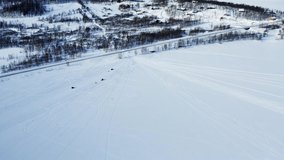 Aerial: An unidentified big group of people drive many snowmobiles on frozen lake, then cross the highway and continue ride in the wild birch forest in Northern Mountains, Joesjo, Lappland, Sweden