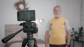modern elderly male blogger maintains a blog about a healthy lifestyle and records video on a mobile phone in the room during a live broadcast