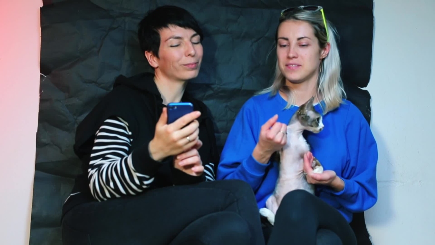 Same-sex partners dance with their cat. Take a selfie on a smartphone.