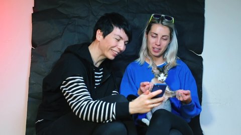 Same-sex partners dance with their cat. Take a selfie on a smartphone.