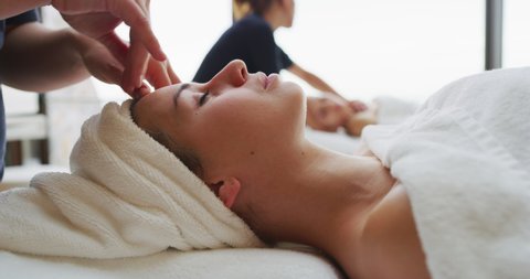 Close up of two young girlfriends with a towel on head are receiving a facial massage and spa treatment for perfect skin in a luxury wellness center.