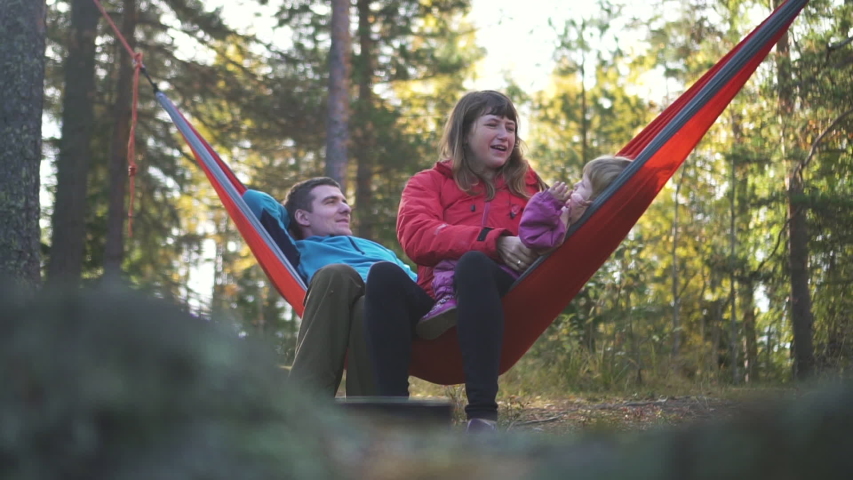 family vacation camping relax. dad, mom, little daughter on hammock together. mother playing with child. concept smiling, posing, vacation, nature