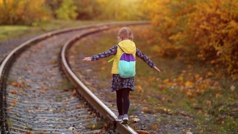 Cute little girl walking on rails in autumn