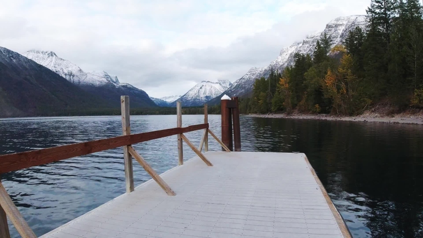 Traveler walks by pier at Lake Mcdonald in Glacier National Park, view of Montana lands, mountains and lake, mountains and forest in a fog, travel around United States