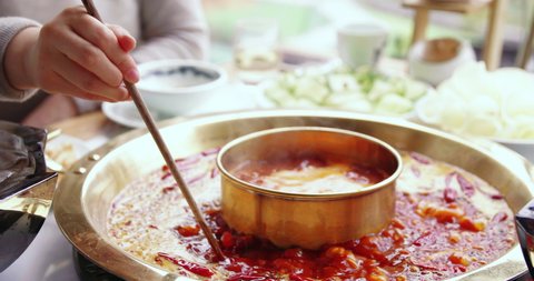 Close up slow motion of people having hotpot typical spicy Sichuan food  at Chengdu China people using chopstick putting food into hot boiling soup traditional way of cooking