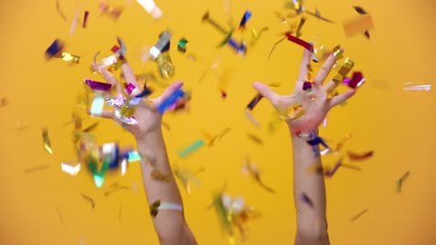 Flying falling colorful confetti isolated over yellow orange background in studio. Holiday party birthday lifestyle Happy New Year 2020 concept. Woman toss up golden shine tinsel show thumbs up.