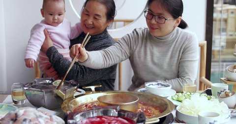 Slow motion of happy Chinese family of three generation having lunch together in the restaurant senior woman holding her baby granddaugher with her daughter eating hotpot Sichuan food at Chengdu China