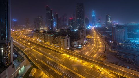Dubai downtown skyline night to day transition aerial timelapse with traffic on highway, UAE. Top view from rooftop of skyscraper with modern towers near intersection of Al Saada street and Financial