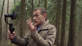 male blogger is recording video on smartphone with gimbal in woods in nature.