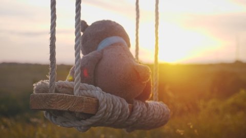 Teddy Bear sitting on the rope swing during sunset. Concept about loneliness.