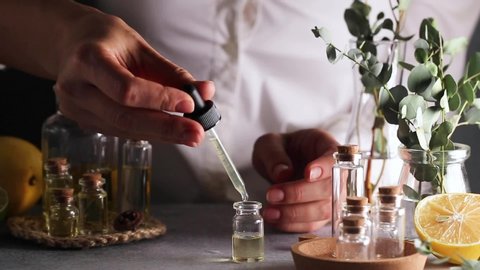 Woman hand pouring eucalyptus essential oil into bottle on grey table