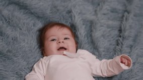 A gorgeous little baby lies on the bed and smiles at the camera . Cute baby smiling and looking in the camera close up .  Beautiful Smiling Baby . Shot on RED EPIC Cinema Camera in Slow Motion .