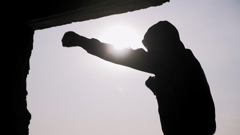 Silhouette of a boxer on a sunset background. Coaches punches. Shadow-boxing. Outdoor workout. Motivational video. 
